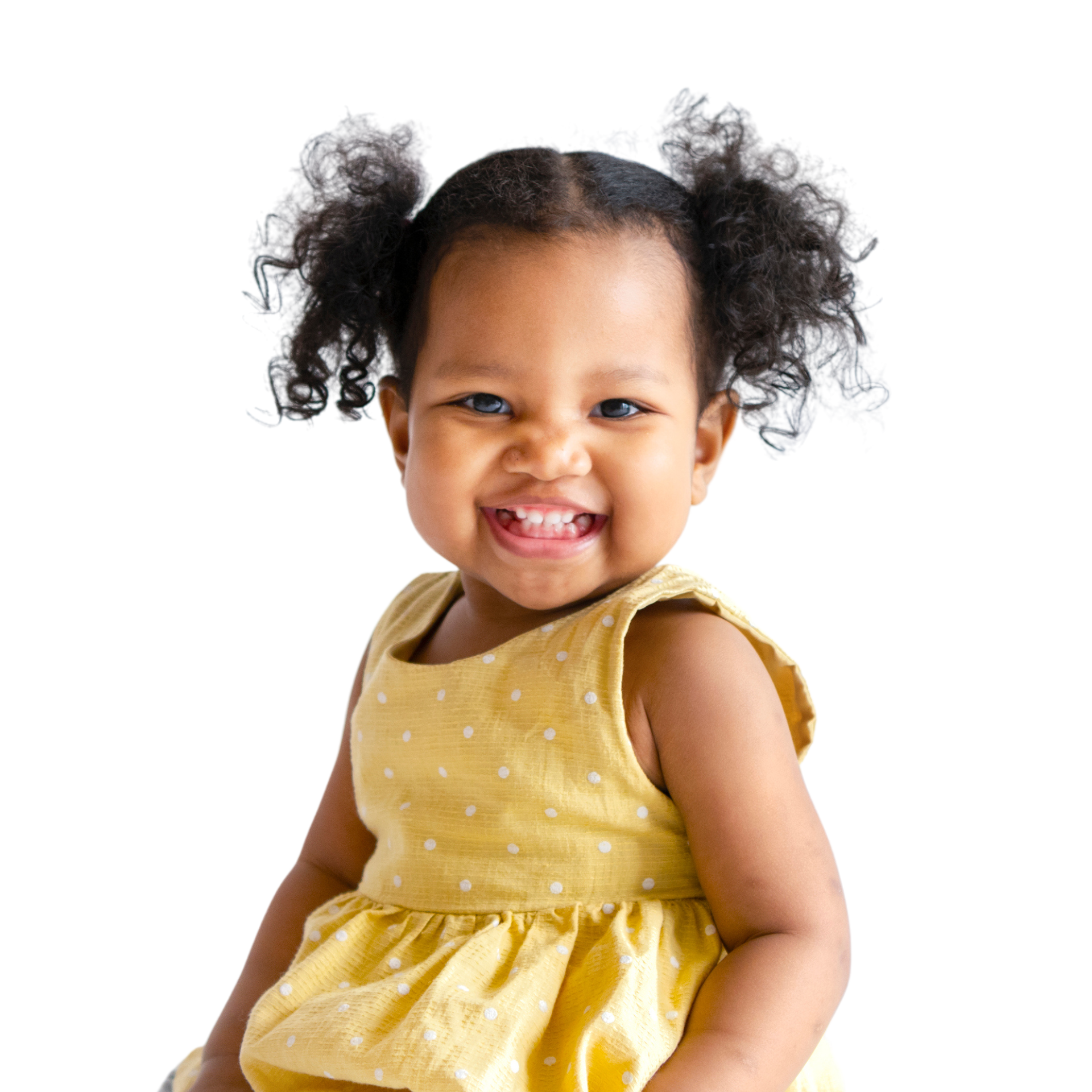 Smiling girl with two curly ponytails wearing a yellow dotted dress smiles 